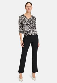 Leopardenmuster Bluse mit V-Ausschnitt, langen Ärmeln, kombiniert mit geraden schwarzen Hosen und hellen Schuhen. Strukturierter Stoff.