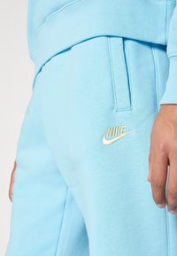 Ljusbl åa sweatpants av mjukt material, med ett elastiskt midjeband, sidofickor och en guld broderad Nike-logotyp.