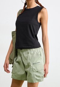 Top negro sin mangas con cuello redondo combinado con pantalones cortos verde claro que cuentan con cintura elástica y bolsillos cargo.