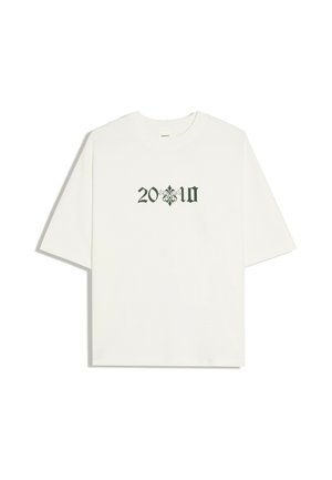 Hvid T-shirt med korte ærmer med sort gotisk stil "20" og "10" tekst adskilt af et dekorativt blomstersymbol midt foran.