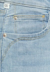 Jean en denim bleu clair avec une poche avant, présentant des coutures jaunes et un détail de bouton argenté. Le tissu a une texture lisse.