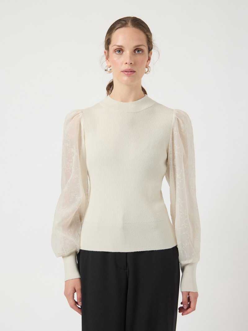 Cream-colored knit top with sheer puff sleeves, high neckline, and fitted bodice. Soft texture with a delicate floral pattern on sleeves.