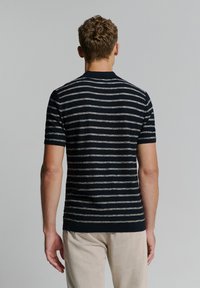 Marineblauw en crèmekleurig gestreept shirt met korte mouwen van gebreid materiaal, voorzien van een ronde hals. Het shirt heeft een aansluitende pasvorm en een ribgebreide zoom. Textuurstof, minimalistische stijl.