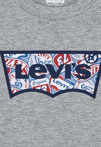 Sweatshirt gris avec un patch logo Levi's bleu marine et des graphismes rétro colorés, comprenant des éléments de design rouges et bleus ainsi que du texte.