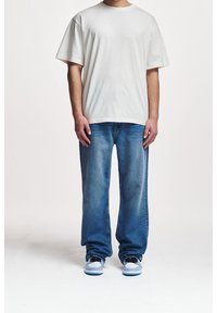 Vit oversize-t-shirt och ljusblå slitna jeans. Sneakersen har vita och ljusblå detaljer. Enfärgad, enkel design.