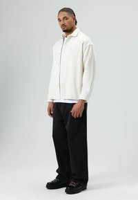 Witte overhemdjas met een losse pasvorm, gecombineerd met zwarte losse jeans en zwarte chunky sneakers met roze veters.