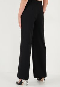 Pantaloni negri cu talie înaltă, cu croială largă, dintr-un material neted. Împreună cu tocuri negre ascuțite și un accent distinctiv de imprimeu de șarpe pe tocuri.