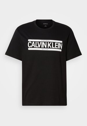 Crna majica kratkih rukava s bijelim logotipom "CALVIN KLEIN NEW YORK" centriranim na prsima, okrugli izrez i oznaka srednje veličine unutar ovratnika.