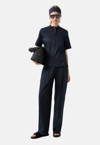 Navy short-sleeve shirt with a high collar, loose-fitting navy trousers, black patterned bag, and flat black sandals with a textured strap.