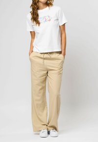Hvid bomulds T-shirt med blomster grafik, parret med beige brede bukser. Bukserne har elastisk talje og sidelommer. Hvide sneakers.