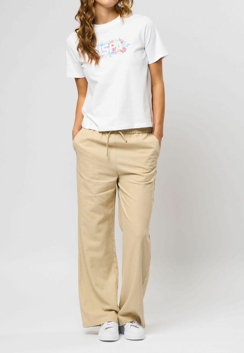 Hvid bomulds T-shirt med blomster grafik, parret med beige brede bukser. Bukserne har elastisk talje og sidelommer. Hvide sneakers.
