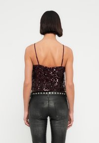 Crop top bordeaux à sequins avec fines bretelles, doté d'une coupe ajustée et d'une fermeture par boutons dans le dos, associé à un pantalon noir taille haute.