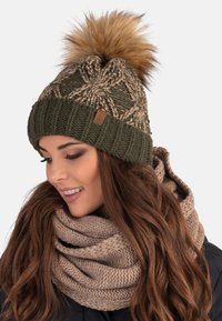 Berretto in maglia di colore verde oliva con un motivo testurizzato e un pompon in pelliccia marrone chiaro in cima; abbinato a una sciarpa in maglia chunky di colore beige.