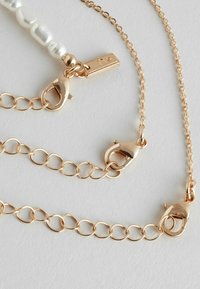 Chaîne de bijoux en ton doré avec trois fermoirs, comportant des maillons ovales et une section avec des perles blanches. Fini lisse et surface brillante.