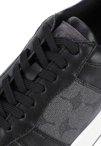Schwarze Sneaker mit einem glatten Lederoberteil, einer strukturierten grauen Einlage, flachen schwarzen Schnürsenkeln und einer weißen Gummisohle.