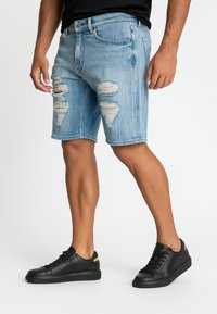 Shorts de mezclilla azul claro con detalles desgastados, bordes deshilachados y un ajuste relajado, combinados con zapatillas negras de textura.