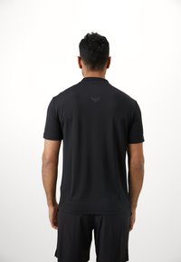 Polo preto com colarinho e mangas curtas, apresentando um logótipo discreto nas costas. O tecido parece suave com uma textura leve.