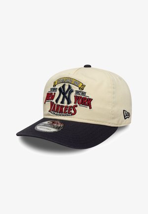 Pet heeft een beige kroon met een donkerblauwe rand. Aan de voorkant is het geborduurde "New York Yankees" logo en oprichtingsjaar in kleurrijke steken te zien.