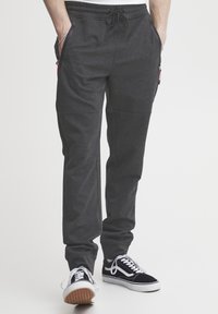 Pantalones joggers grises de tejido texturizado, con cintura elástica y cordón, bolsillos laterales, y combinados con zapatillas negras y blancas.