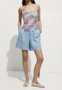 Camisola de cuadros ligera con colores pastel, combinada con pantalones cortos azul claro a medida con bolsillos; completado con zapatos planos beige.