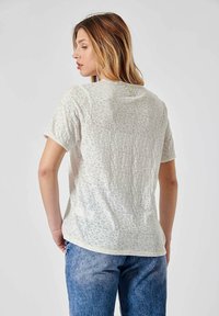 T-shirt à manches courtes, beige clair, avec un imprimé animal discret, encolure ronde et ourlets cousus, associé à un jean en denim bleu.