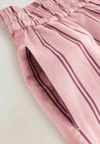 Ljust rosa byxor med vertikala mörkrosa ränder, med ett samlat elastiskt midjeband och sidospalter för ökad ventilation.