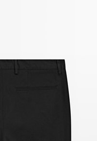 Zwarte formele broek met de achterkant van de tailleband, riemlussen en een enkele paspelzak op een witte achtergrond.