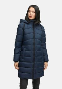 Mujer vistiendo un abrigo de invierno acolchado con capucha en azul marino, con cremallera frontal y bolsillos, de pie con las manos relajadas a los lados, mirando hacia la izquierda.