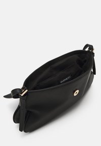 Sac à main en cuir noir avec une texture lisse, une fermeture à bouton doré et une étiquette intérieure. Équipé de deux courtes poignées de chaque côté.
