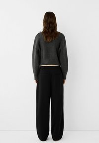 Pull en tricot gris cropped avec ourlet côtelé porté sur un pantalon large taille haute noir. Texture lisse et silhouette décontractée.