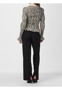 Karierte Bluse mit einem gerüschten Saum und Ärmeln, kombiniert mit schwarzen taillierten Hosen mit Schlitzen am Saum. Glattes Material, figurbetontes Design.