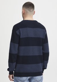 Pulover ribbed bleumarin cu dungi orizontale în nuanțe variate de albastru. Are mâneci lungi și un guler rotund.