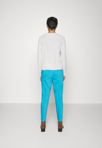 Pull-over rose clair, texture douce, associé à un pantalon slim bleu turquoise vif et des bottines marron à talon bloc.