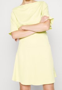 Vestido amarillo claro con mangas cortas, escote redondo, falda de vuelo, hecho de una tela suave, con un detalle atado en la cintura.