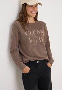 Sweatshirt marron avec le texte "CLEAR VIEW", col rond, manches longues, coupe décontractée, associé à un pantalon noir. Mélange de coton doux, design minimal.