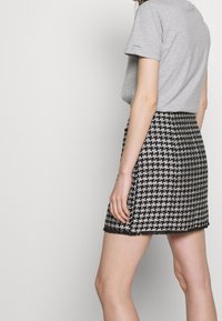 Šedé tričko s krátkým rukávem spojené s černobílou minisukní se vzorem pepito. Sukně má třásňový lem a strukturovanou látku.