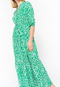 Grönmönstrad maxiklänning som har ett lätt material, V-ringning, korta ärmar, cinchad midja och en utsvängd kjol med en lager på lager-kant.