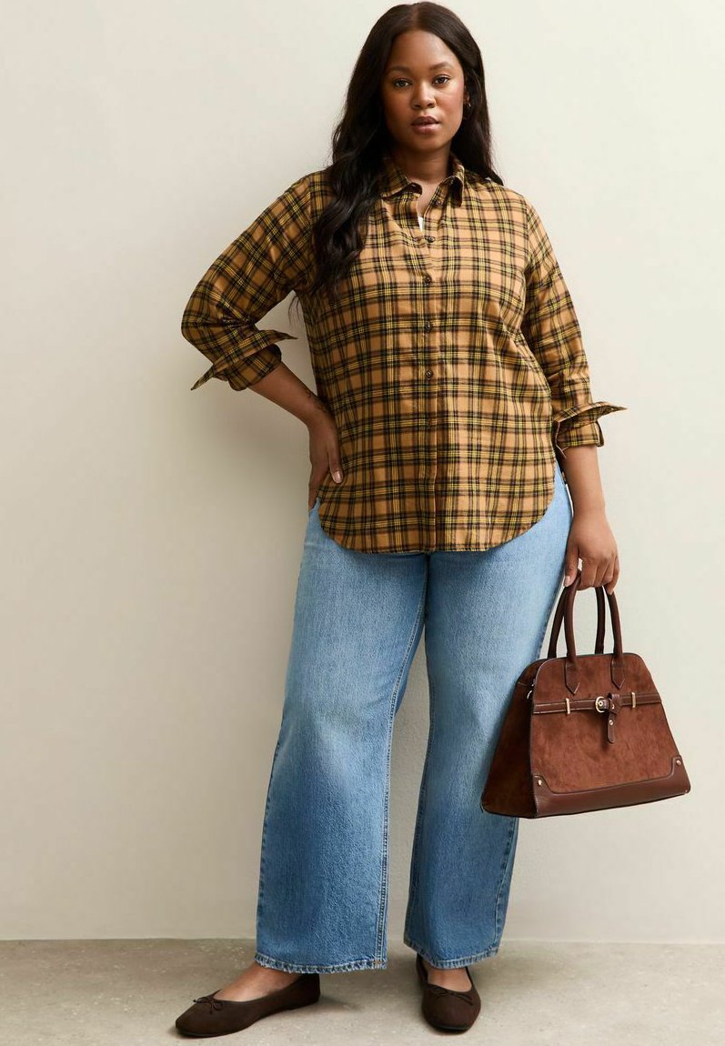 Camisa de cuadros con botones en tonos amarillos y marrones, combinada con jeans de pierna ancha en azul claro. Los accesorios incluyen un bolso marrón y zapatos planos oscuros.