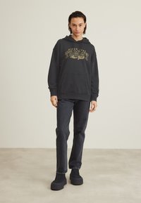 Hanorac negru cu logo "TOMMY" de culoare aurie, prevăzut cu un buzunar frontal, asortat cu blugi închiși la culoare și pantofi platform negri. Material neted, croială lejeră.