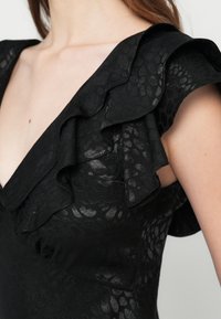 Juoda suknelė su raukiniais rankovėse, puošta tekstūruotu gyvūnų raštu. V formos iškirpte paryškintas audinio subtilus blizgesys ir sudėtingas detalizavimas.