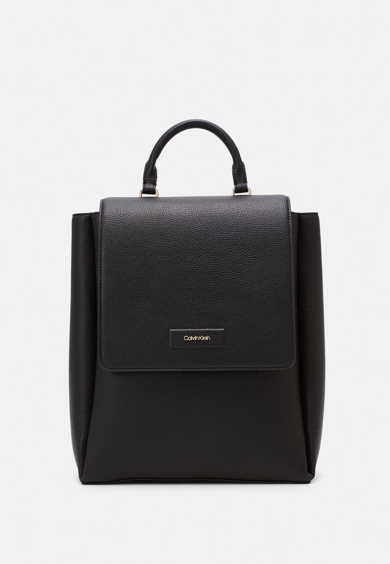 Sac à dos en cuir noir avec une poignée supérieure et une fermeture par rabat à l'avant, avec une petite plaque logo Calvin Klein sur le devant.