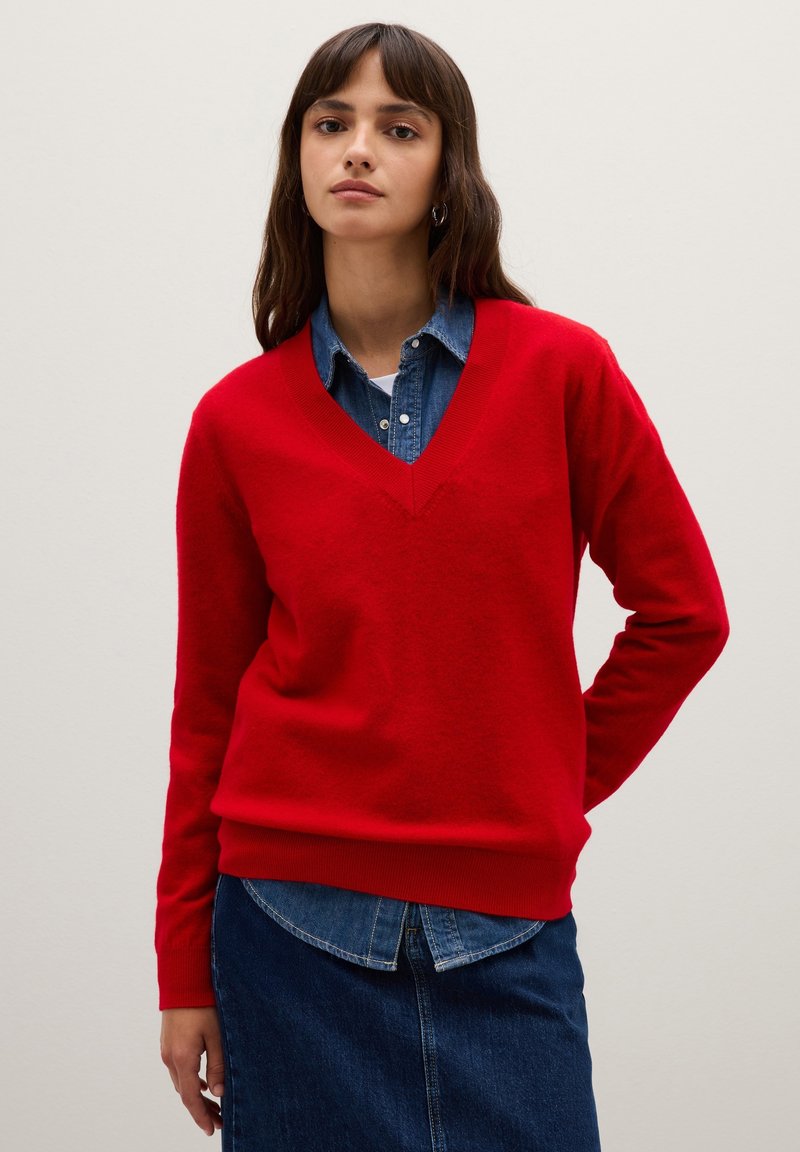Cardigan rosso a V realizzato in morbido tessuto, con polsini e orlo a coste, abbinato a una camicia di denim sotto.