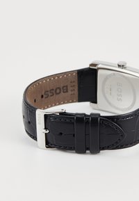 Montre avec bracelet en cuir noir, dotée d'un boîtier rectangulaire en argent, d'un cuir texturé et d'une boucle en métal gravée "BOSS".