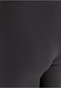Leggings noirs en tissu lisse et extensible, avec une coupe ajustée et une taille sans couture pour un confort et une flexibilité optimaux.