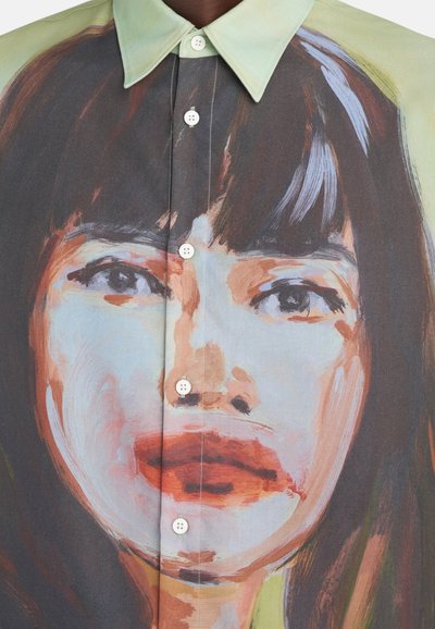 Chemise à boutons présentant un grand imprimé artistique d'un visage. Le tissu est léger avec un dégradé de couleurs, principalement vert et marron, à texture lisse.