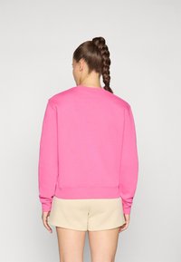 Pullover genser i lys rosa, laget av myk stoff, har lange ermer og en avslappet passform. Bakfra vises rund hals og ribbestrikket kant.