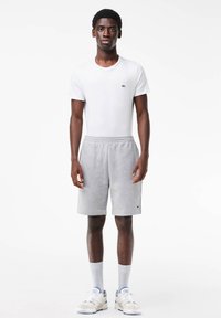 White short-sleeve t-shirt with green logo; gray, knee-length shorts with elastic waistband; white socks and sneakers. Simple, casual outfit.