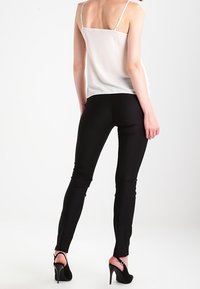 Vit ärmlös topp med tunna remmar som kombineras med åtsittande svarta byxor, som visar en slät tygkvalitet och en elegant silhuett. Svarta högklackade skor fulländar outfiten.