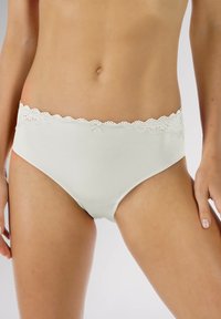 Witte katoenen slip met een geschulpte kantentailleband, een klein strikje aan de voorkant en een zachte structuur. Ontworpen voor comfort en pasvorm.