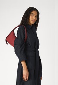 Red nylon handbag with a triangular design and a single shoulder strap, paired with a black pinstriped dress featuring a belted waist.
